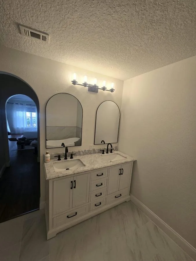 Bathroom finished in porcelain tile with a double vanity and arched mirrors