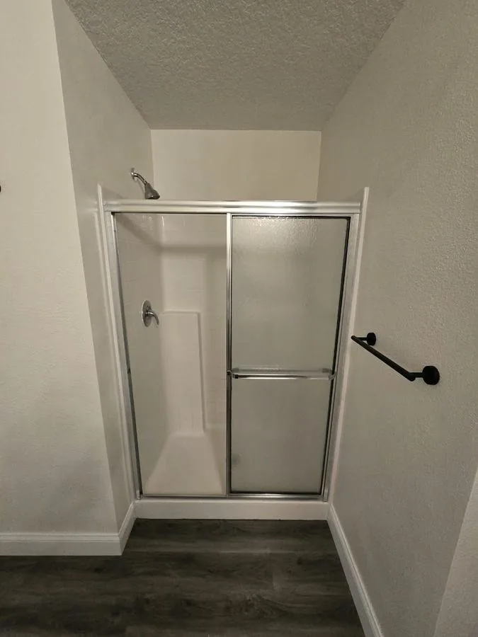The shower before the job: a prefab acrylic stall with an aluminum sliding door and dark vinyl plank floor