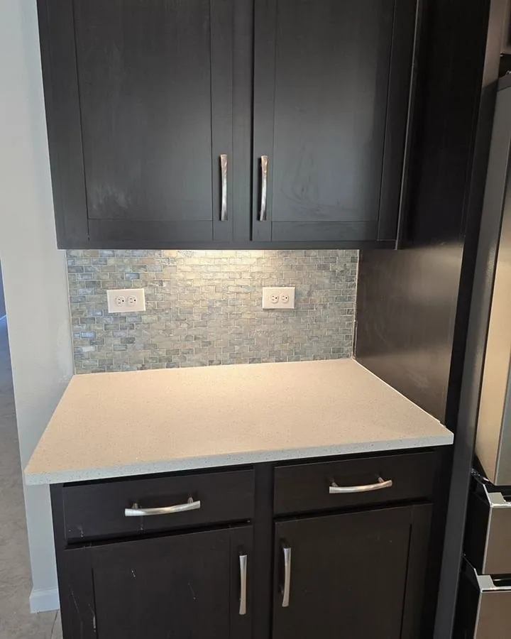 Kitchen backsplash in a blue-green glass mosaic between dark upper cabinets