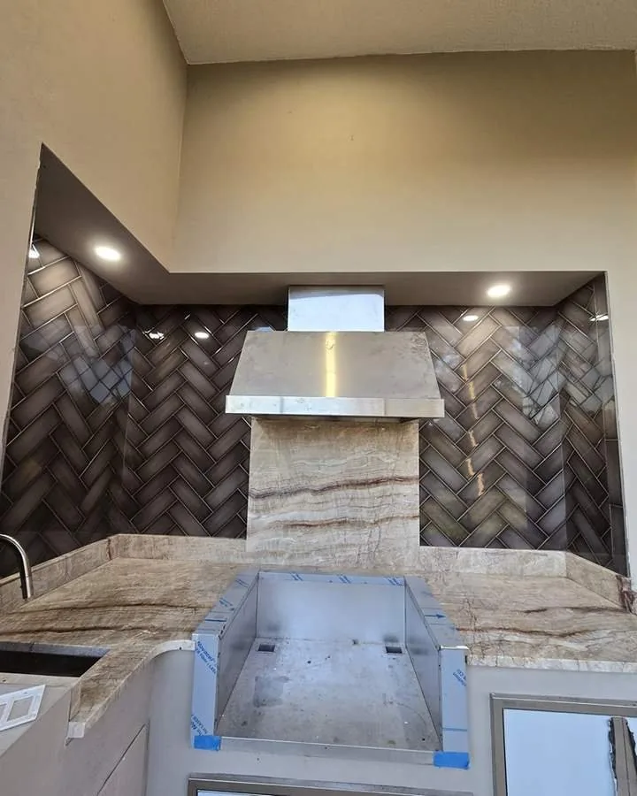 Kitchen backsplash laid in a dark herringbone pattern behind a stainless range hood