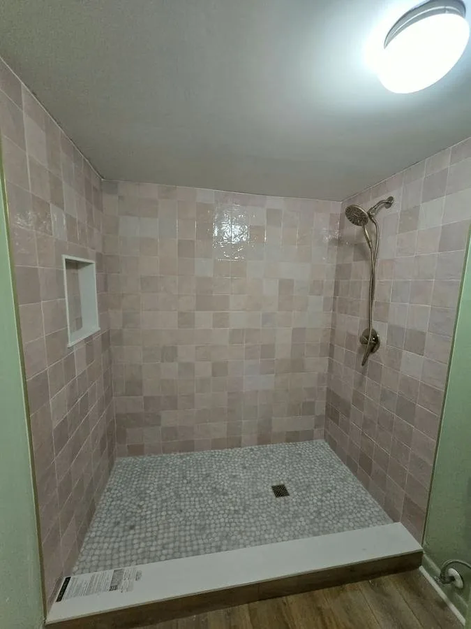 Shower tiled in warm square wall tile with a mosaic floor and a built-in niche