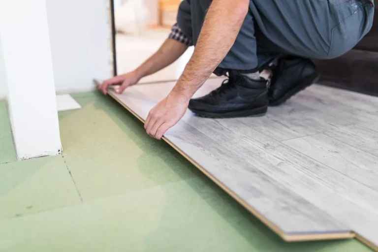 Installer laying a luxury vinyl plank over underlayment, fitting the board against the wall